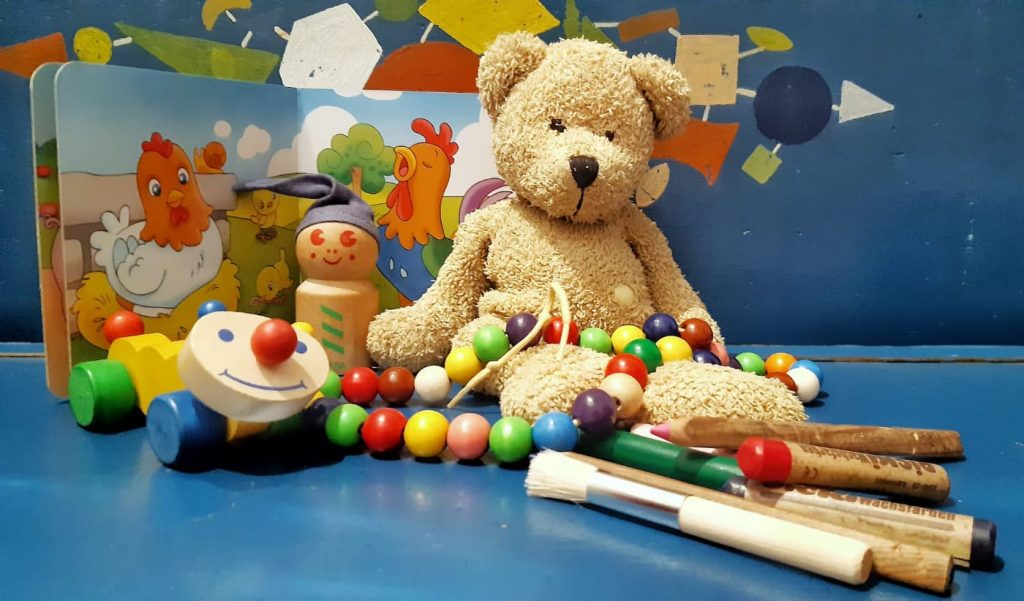 Holzspielzeug, Teddybär, Wachsmalstifte, Bilderbuch auf blauer Kinderbank